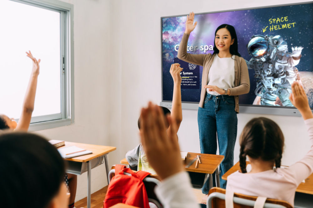 Asian school teacher with students raising hands. Young woman working in school with arm raised, school children putting their hands up to answer question, enthusiasm, eager, enjoyment