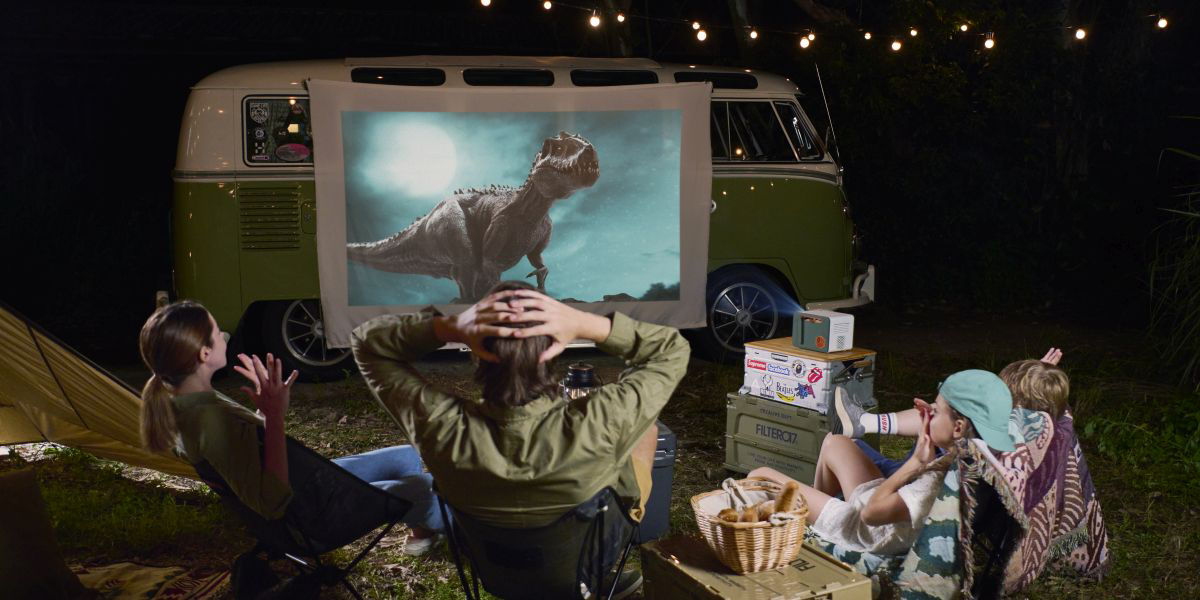 A family of four watching movie while camping using an outdoor projector