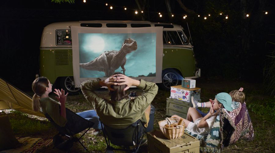 A family of four watching movie while camping using an outdoor projector