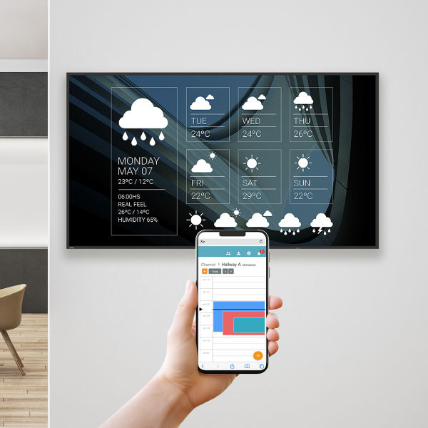 A hand holding a smartphone to remotely schedule and manage content on a BenQ signage display via X-Sign Manager with AWS-grade security.