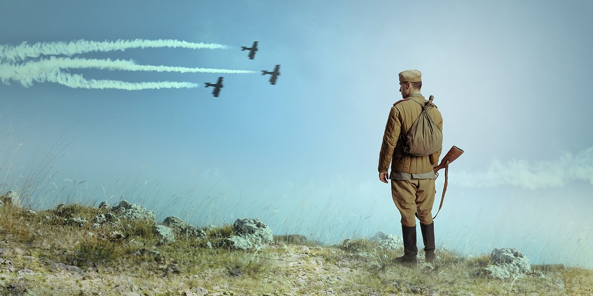 A soldier standing in the field with three battle jets flying over the sky